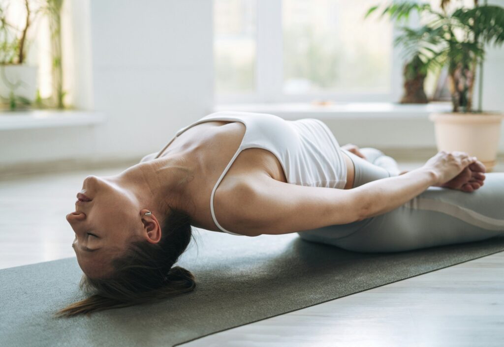 Posture de yoga réalisée par une personne sur un tapis avec un fond lumineux et apaisant.