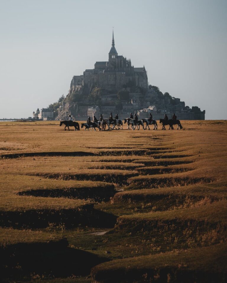 A beautiful scene of horseback riders with Mont-Saint-Michel in the background.