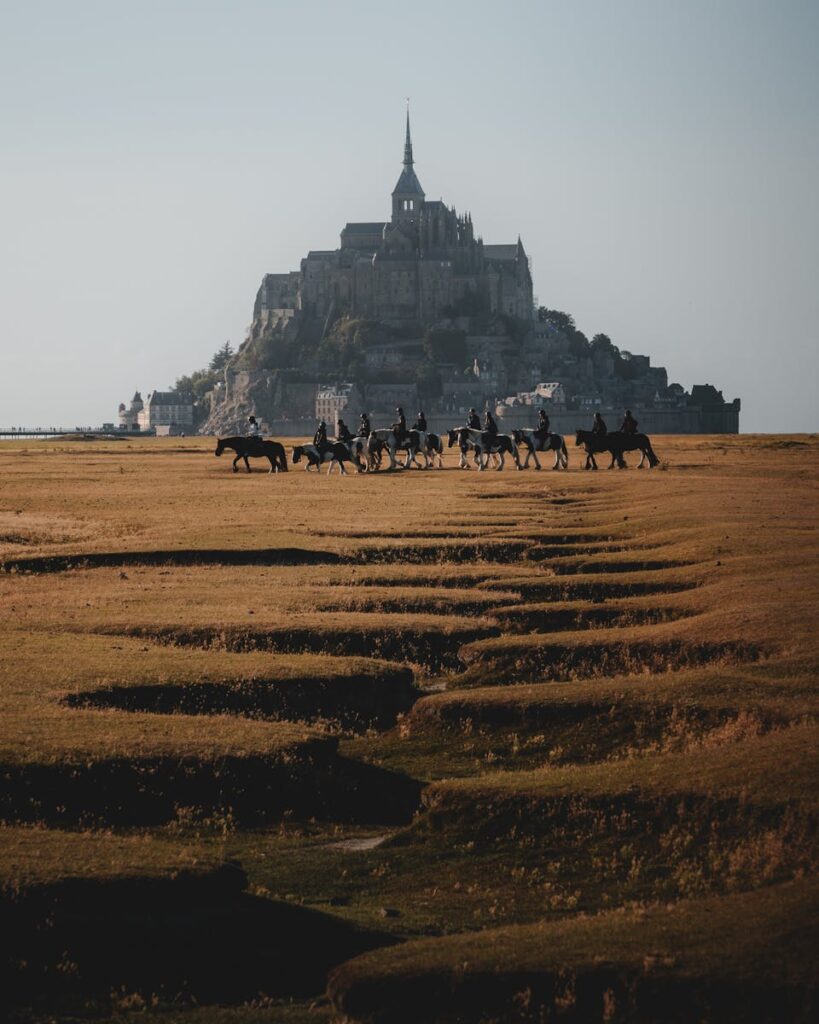 A beautiful scene of horseback riders with Mont-Saint-Michel in the background.
