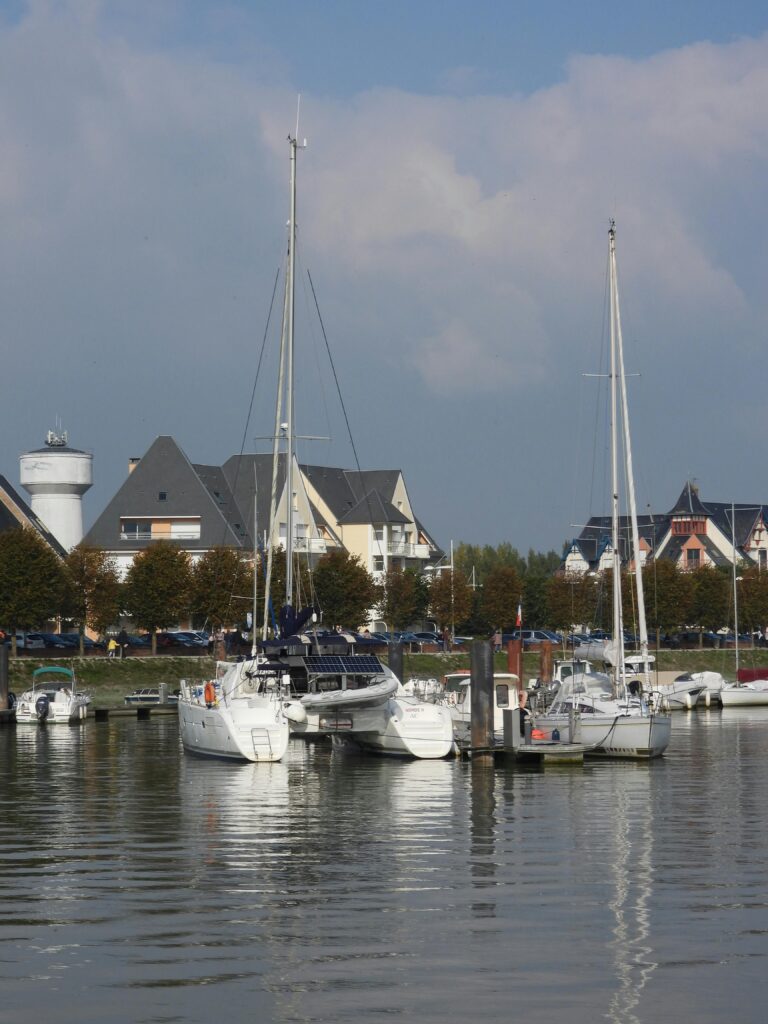 Sailboats docked at Le Crotoy marina with scenic village backdrop.